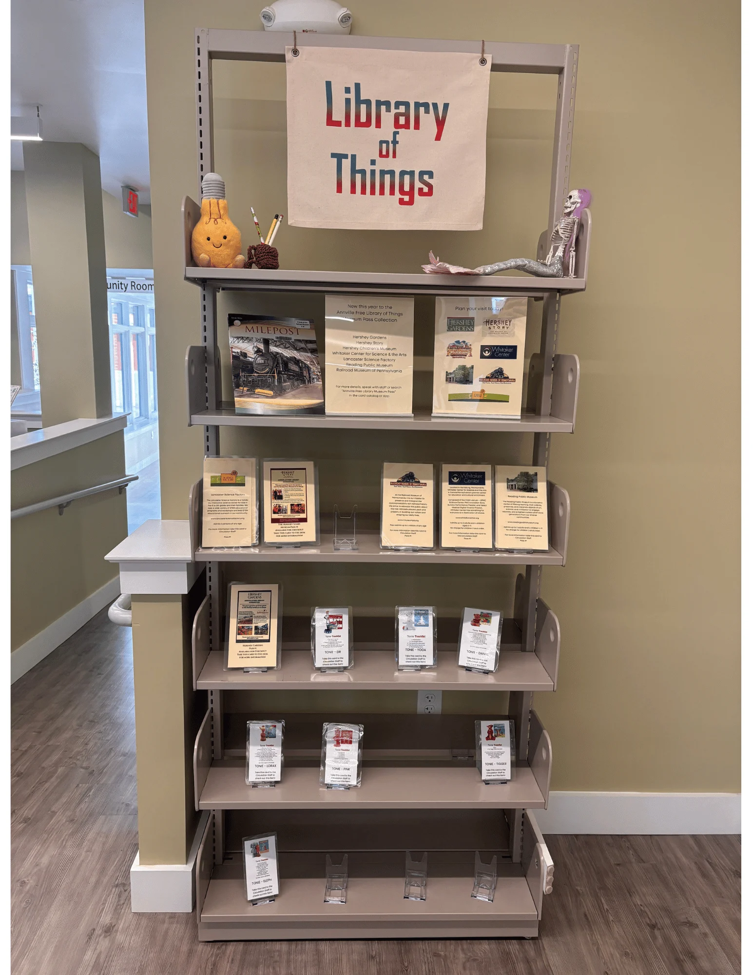 a metal shelving unit with a large sign that reads "library of things" and several shelves with museum passes and TONIE toys